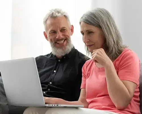 Smiling older couple sitting on a couch using a laptop together