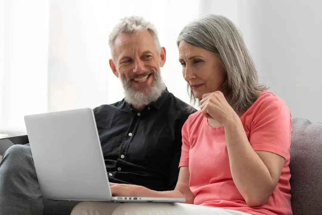 Smiling older couple sitting on a couch using a laptop together