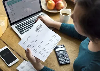 Person reviewing a utility or tuition bill next to a laptop and calculator, preparing for an international payment.