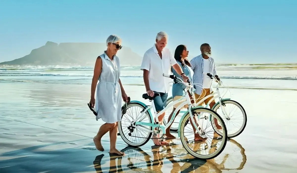 Group of seniors walking with bikes along a sunny beach, representing snowbirds enjoying retirement in the U.S.