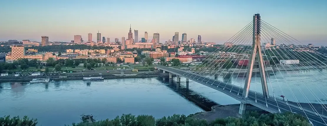 Scenic view of Warsaw's city skyline at sunset with the Świętokrzyski Bridge spanning the Vistula River in the foreground, symbolizing Poland’s modern urban landscape
