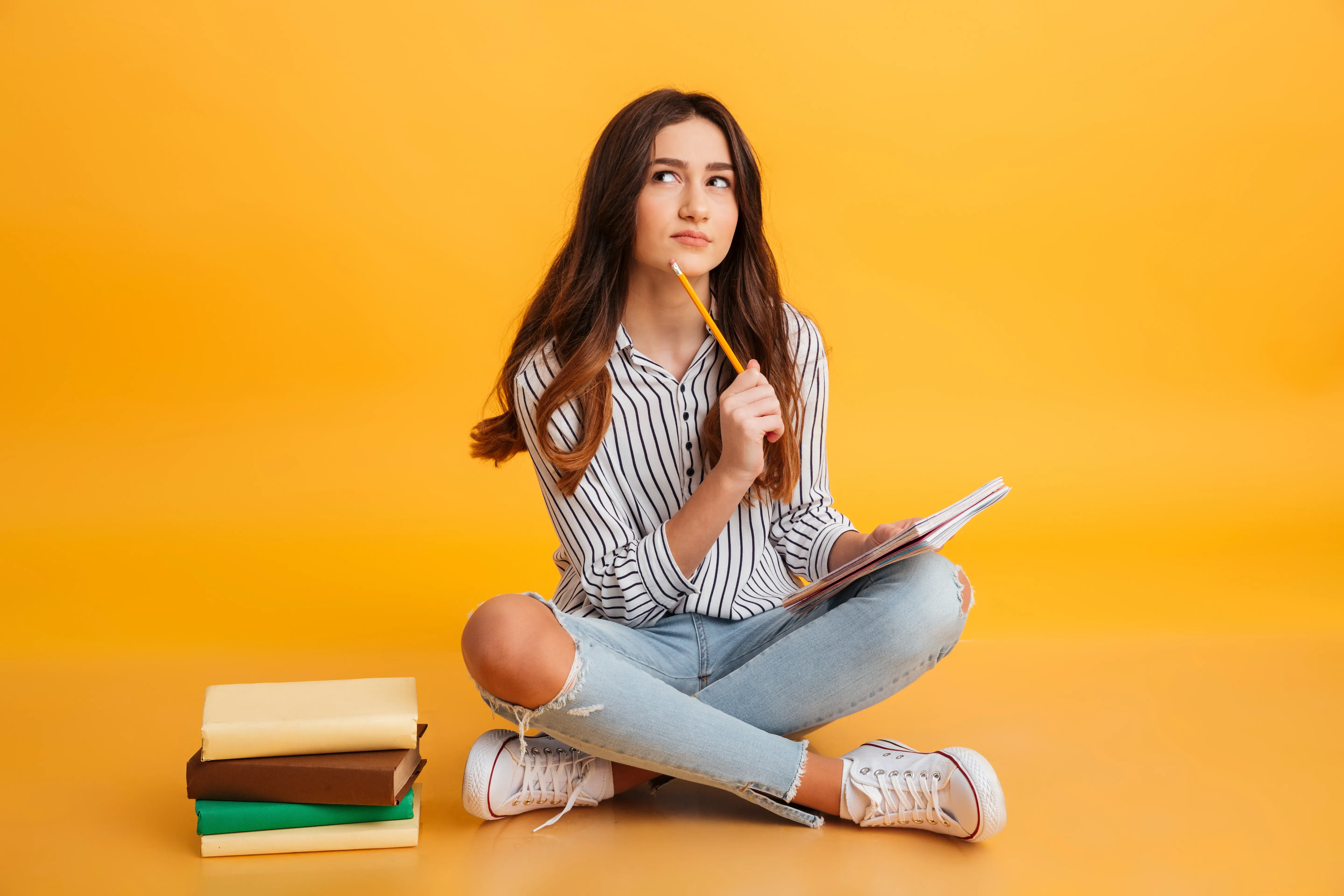 Student sitting with books and notebook, planning studies abroad and considering the cost of studying in the US.
