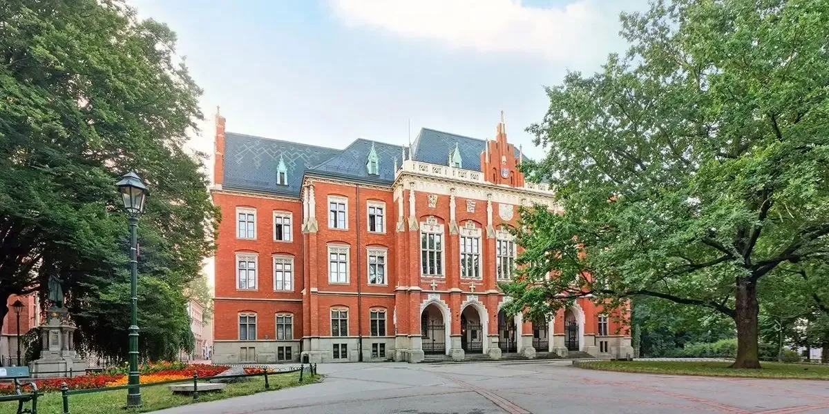 Red brick Collegium Novum building of Jagiellonian University framed by trees and flowerbeds. Use MTFX to pay tuition from Canada to Poland securely with fast delivery and competitive CAD to PLN rates.