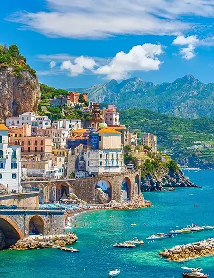 Scenic coastal town in Italy with colorful cliffside buildings, turquoise waters, boats, and mountains in the background