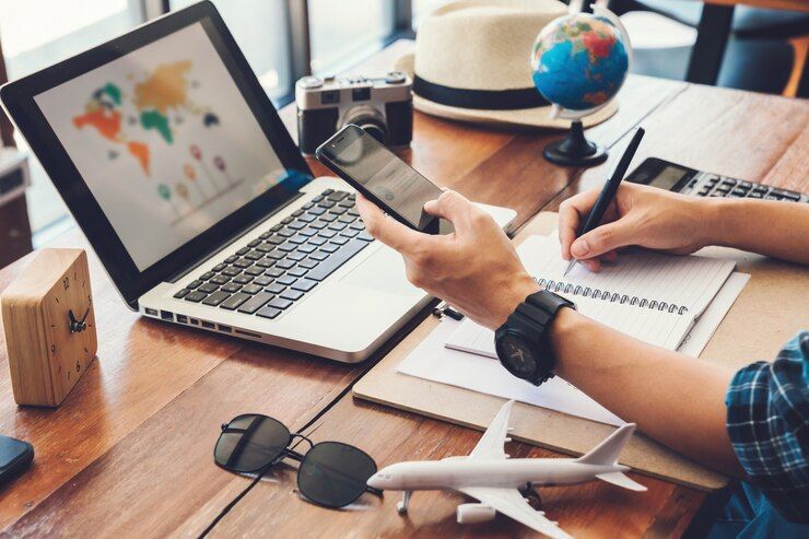 Person planning international travel at a desk with a laptop, smartphone, globe, model airplane, and notepad, representing global trip coordination.