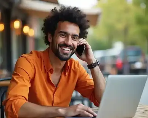 Smiling man using laptop and phone to send money to France online from Canada