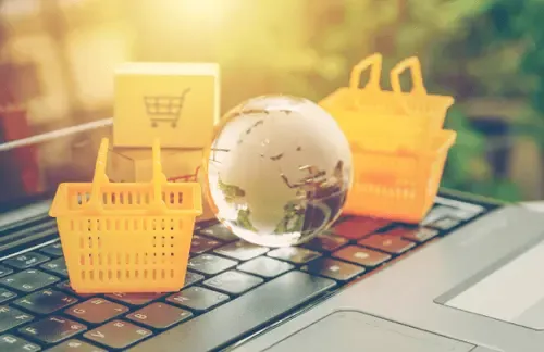 Mini shopping carts, cardboard boxes, and a glass globe on a laptop keyboard representing global eCommerce and international online payments.