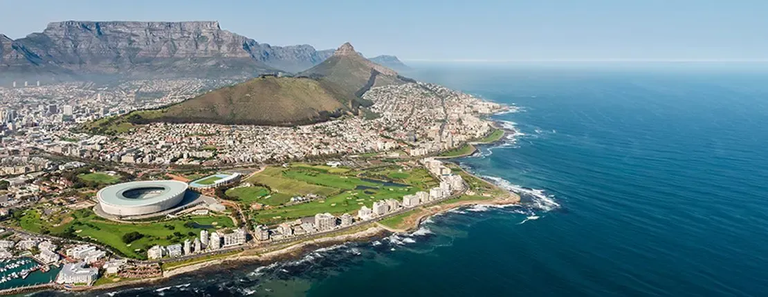 Aerial view of Cape Town, South Africa, featuring Table Mountain, the coastline, and the Cape Town Stadium.