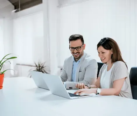 Smiling man and woman working together on laptops in a bright, modern office setting.